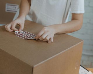 Woman preparing shipment by applying a 'fragile' sticker on a cardboard box in a warehouse.